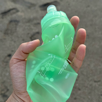 Green silicone water bottle pouch held in a hand with a sandy background